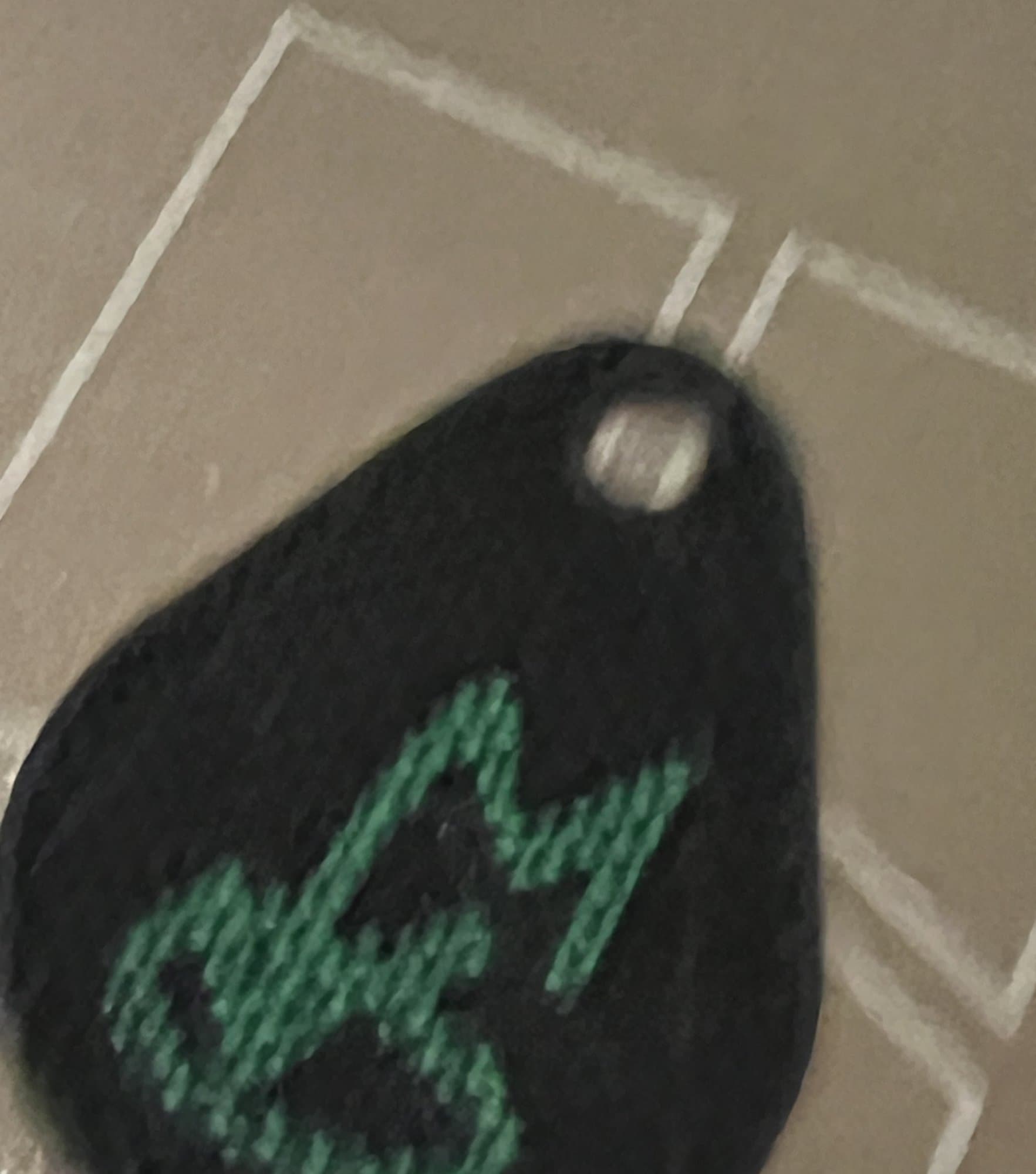 The first test, 22.10.2024: a flat teardrop tag, black with a green logo, still on the printer bed.