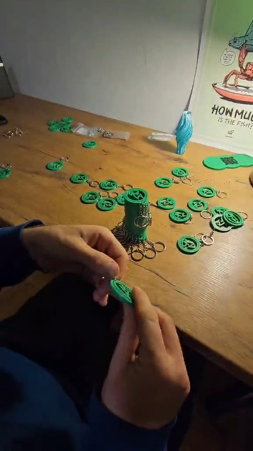 The finished run on the desk: keychains with key rings, one in hand before its ring goes on (frame from a video, 04.12.2024).