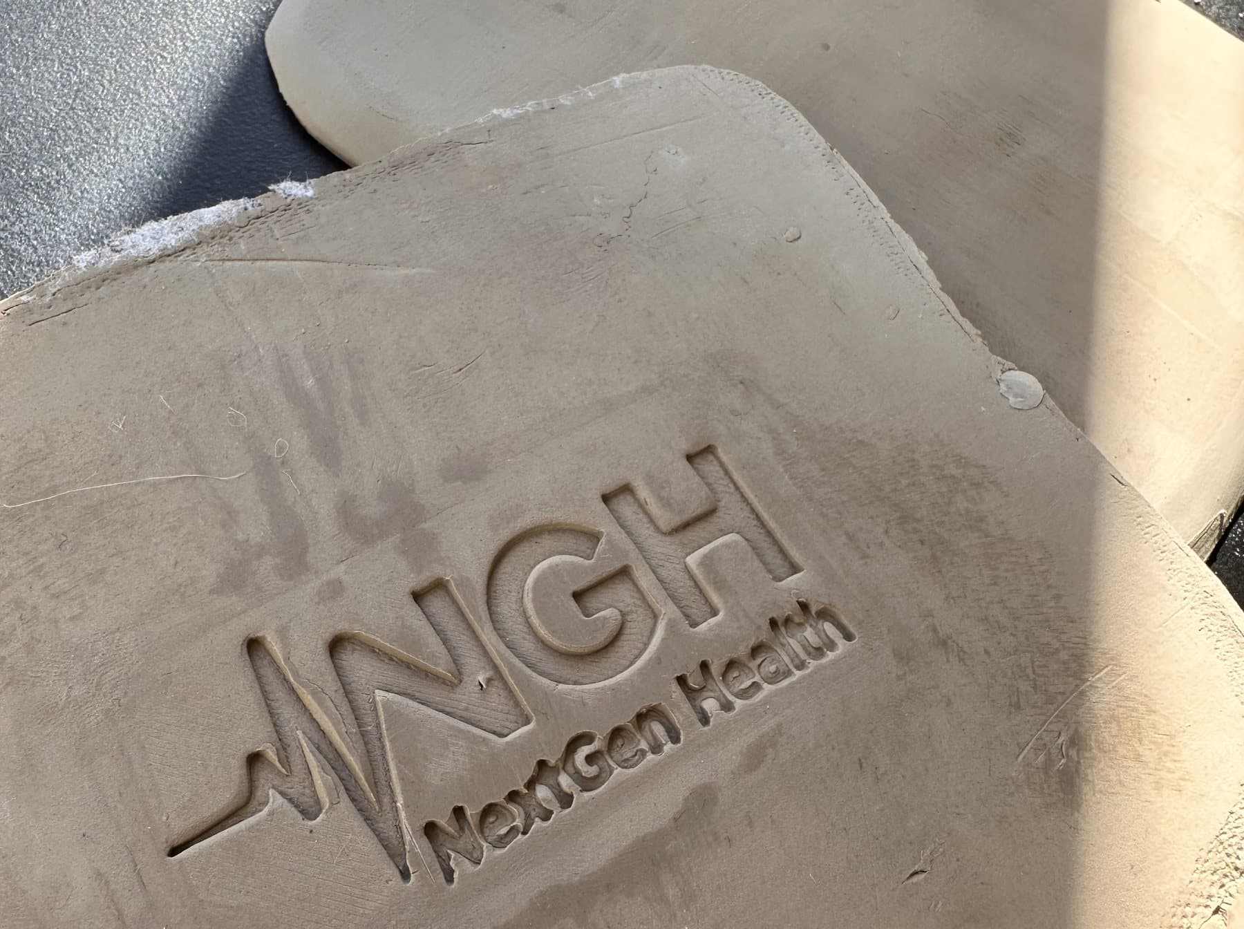 Odcisk logo NextGen Health w surowej glinie, razem z podpisem, który na starcie był na granicy czytelności.