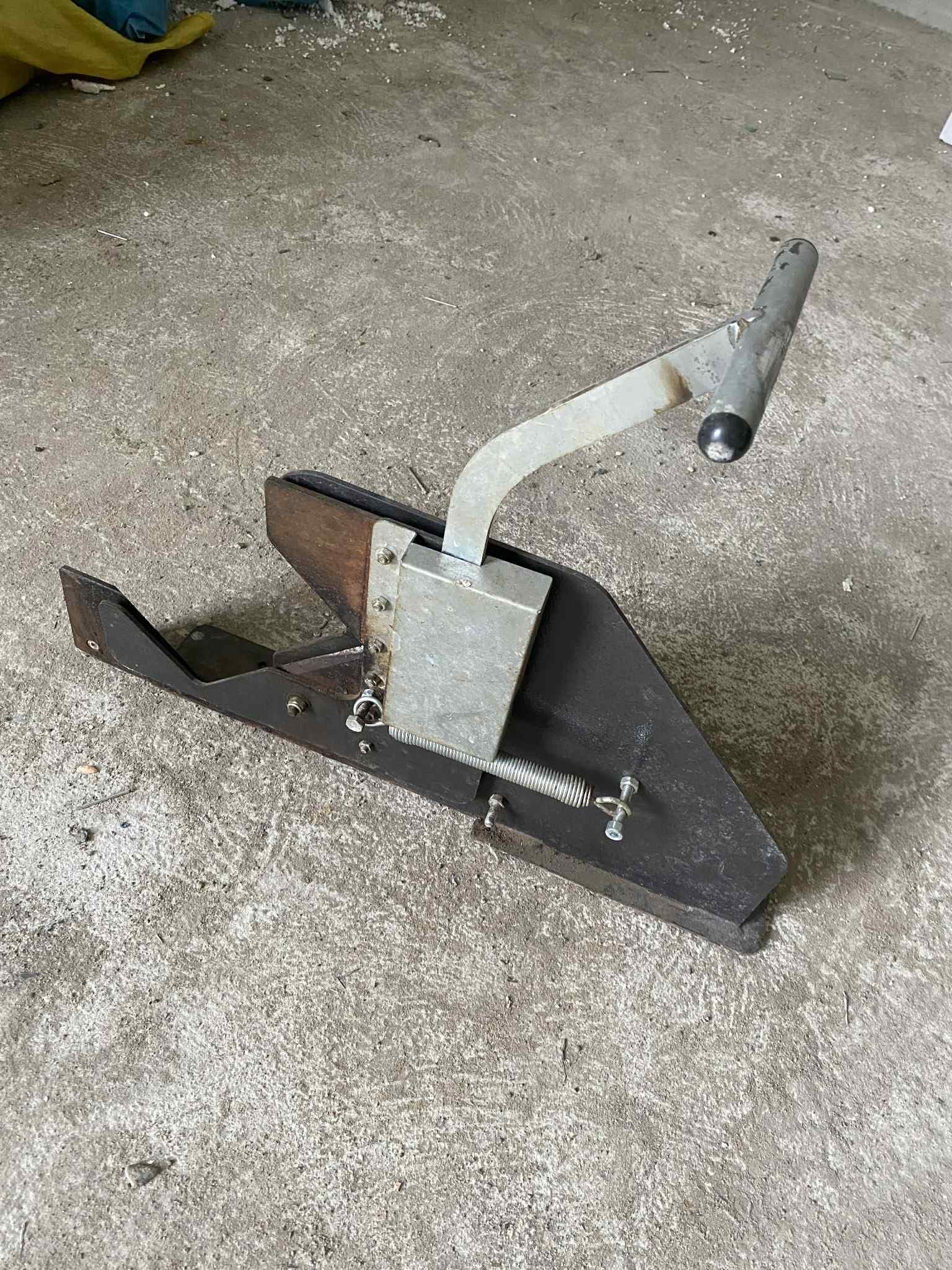 Widok z boku mechanizmu dźwigni i bloku zacisku z ostrzem, na betonowej posadzce.